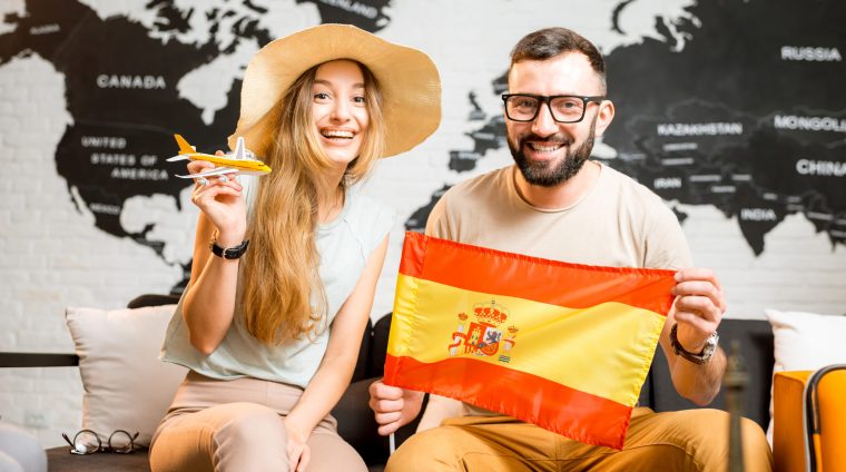 Young couple sitting with spanish flag at the travel agency office on the world map background prepairing for a trip to Spain