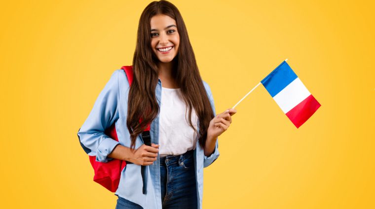 Cheerful caucasian young student woman, with France flag, combines patriotism with academia, isolated on yellow background. Lifestyle, national pride and exchange study, learning french